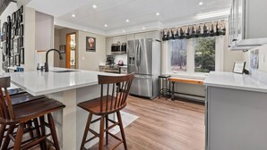 Una cocina moderna con una isla central, electrodomésticos de acero inoxidable y un amplio ventanal con vistas a árboles.