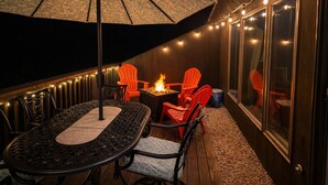 Un patio exterior con una mesa redonda, sillas, un hogar y luces colgantes.