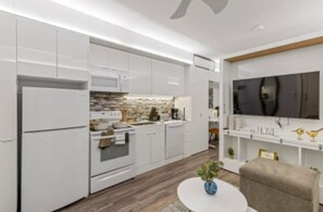A modern kitchen with white cabinetry, a built-in oven, and a microwave. There is a dining area with a round table and a chair.
