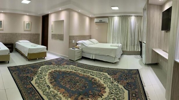 A hotel room with two beds, a large decorative rug, a TV, and a bathroom with a shower. - Hotel Monte Líbano (Paranaguá)
