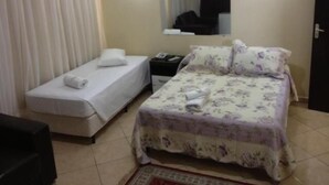 A hotel room with a bed, a bedside table, a mirror, and a door. - Hotel Monte Líbano (Paranaguá)