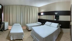A hotel room with a curved ceiling, two single beds, a desk with a chair, a TV, and a large window with curtains. - Hotel Monte Líbano (Paranaguá)