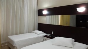 A hotel room with two beds, a nightstand with a phone, and a large mirror on the wall. - Hotel Monte Líbano (Paranaguá)