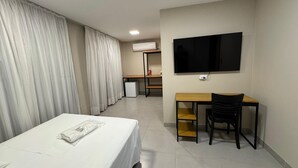 A hotel room with a bed, a desk, a chair, a television, and an air conditioning unit. - Hotel Monte Líbano (Paranaguá)
