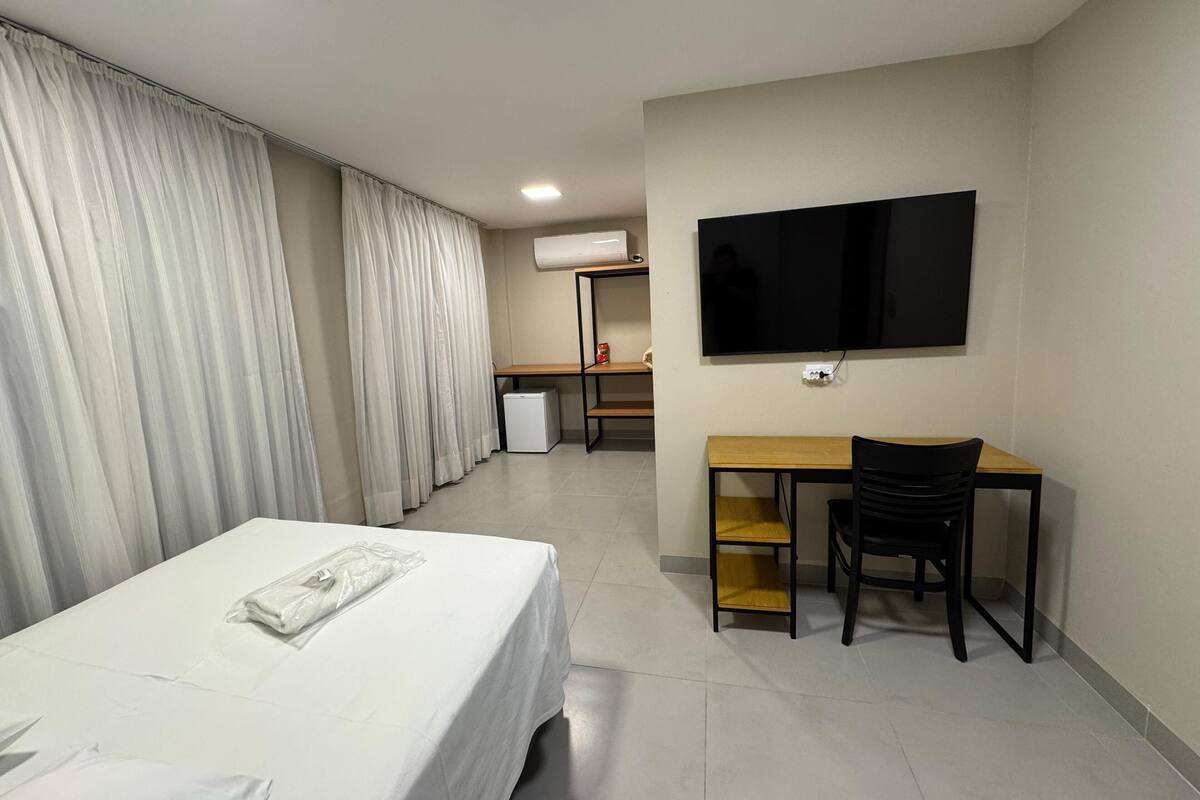 Habitación de hotel con cama, escritorio, silla, televisor y aire acondicionado.