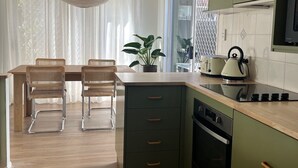 Une cuisine avec un coin repas, un plancher en bois, des armoires vertes, un four à micro-ondes et une plante en pot.