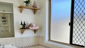 Une salle de bain avec une baignoire, un lavabo, une fenêtre donnant sur un beau paysage et des étagères remplies de produits de toilette.