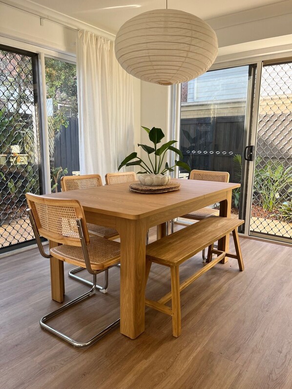 A wooden dining table with chairs, a hanging light fixture, and a potted plant.
