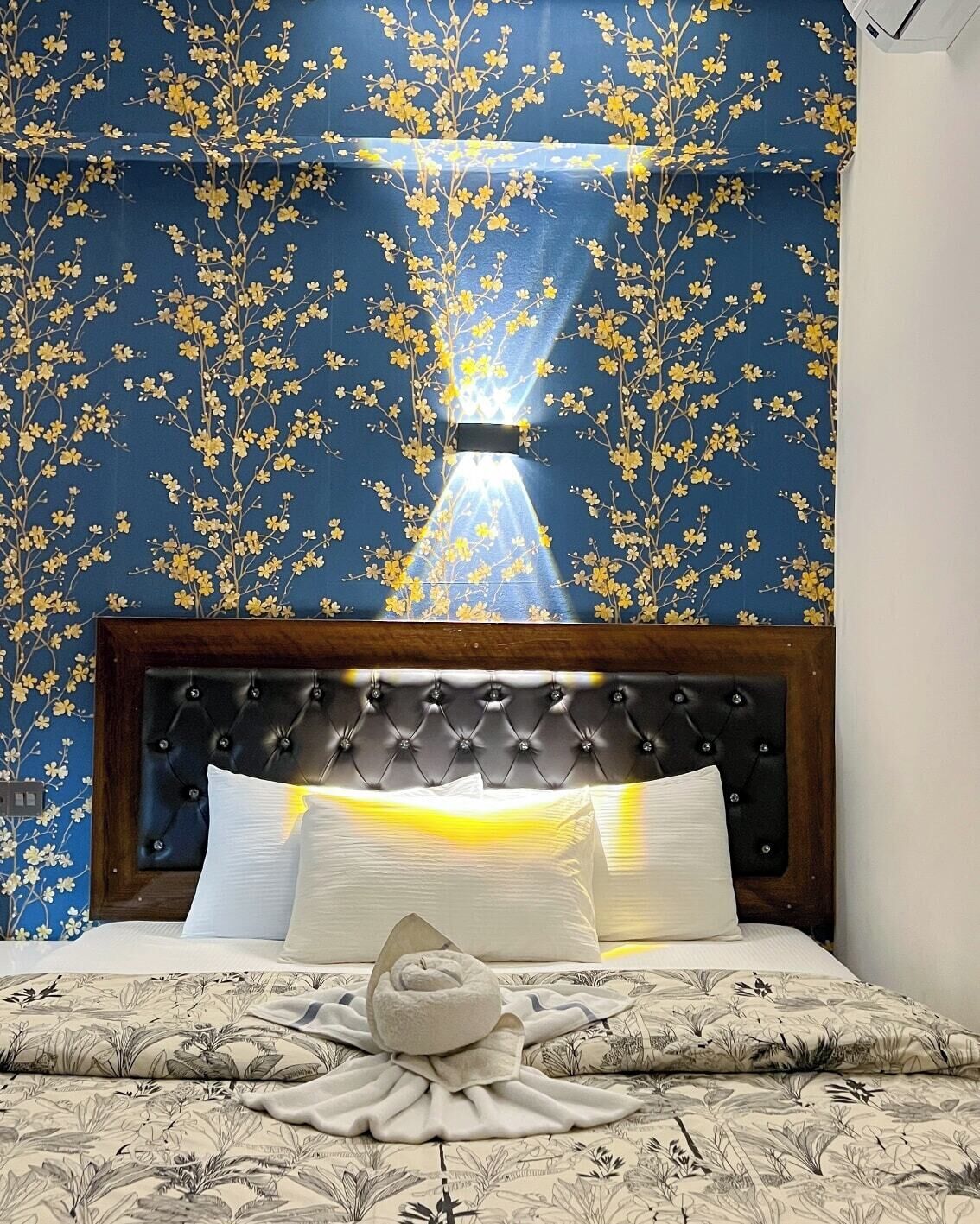 Un dormitorio con cabecera capitonada, cama con ropa de cama blanca y pared con estampado floral.
