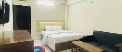 A hotel room with a bed, a sofa, a small table, a ceiling fan, and a television.
