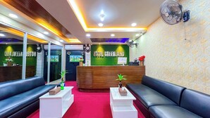 A hotel reception area with a wooden reception desk, two black leather sofas, a red carpet, and a green wall with the hotel's name. - Hotel Green Land Bandarban (Bandarban)