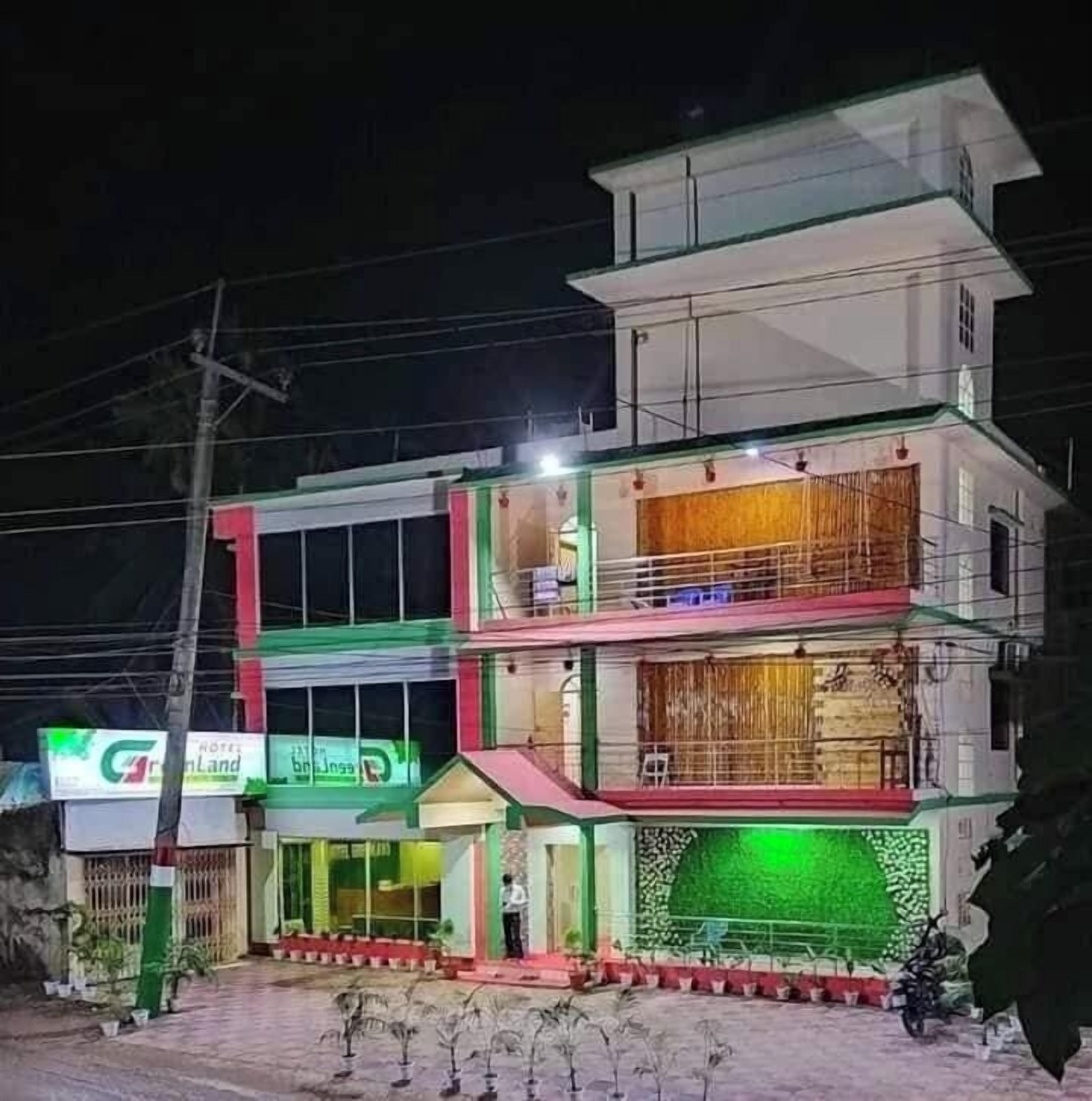 Um hotel com vários andares, fachada iluminada em verde, varanda vis ível no andar superior e placa indicando um restaurante no térreo.