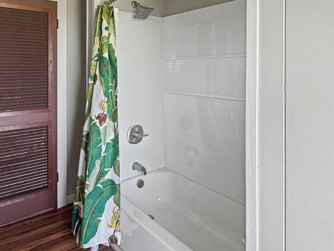 Een badkamer met een bad, douche en een raam met zonwering.