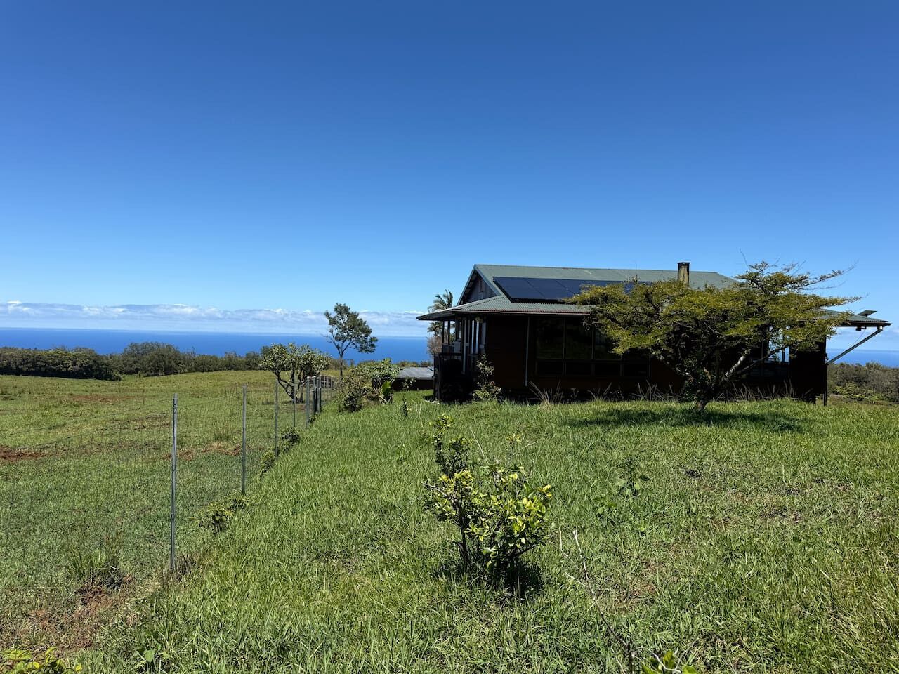 Ein Haus mit einer Solaranlage auf dem Dach, umgeben von einer Wiese und einem Zaun.