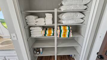 Un armadietto con scaffali che contengono asciugamani, cuscini e articoli da bagno.