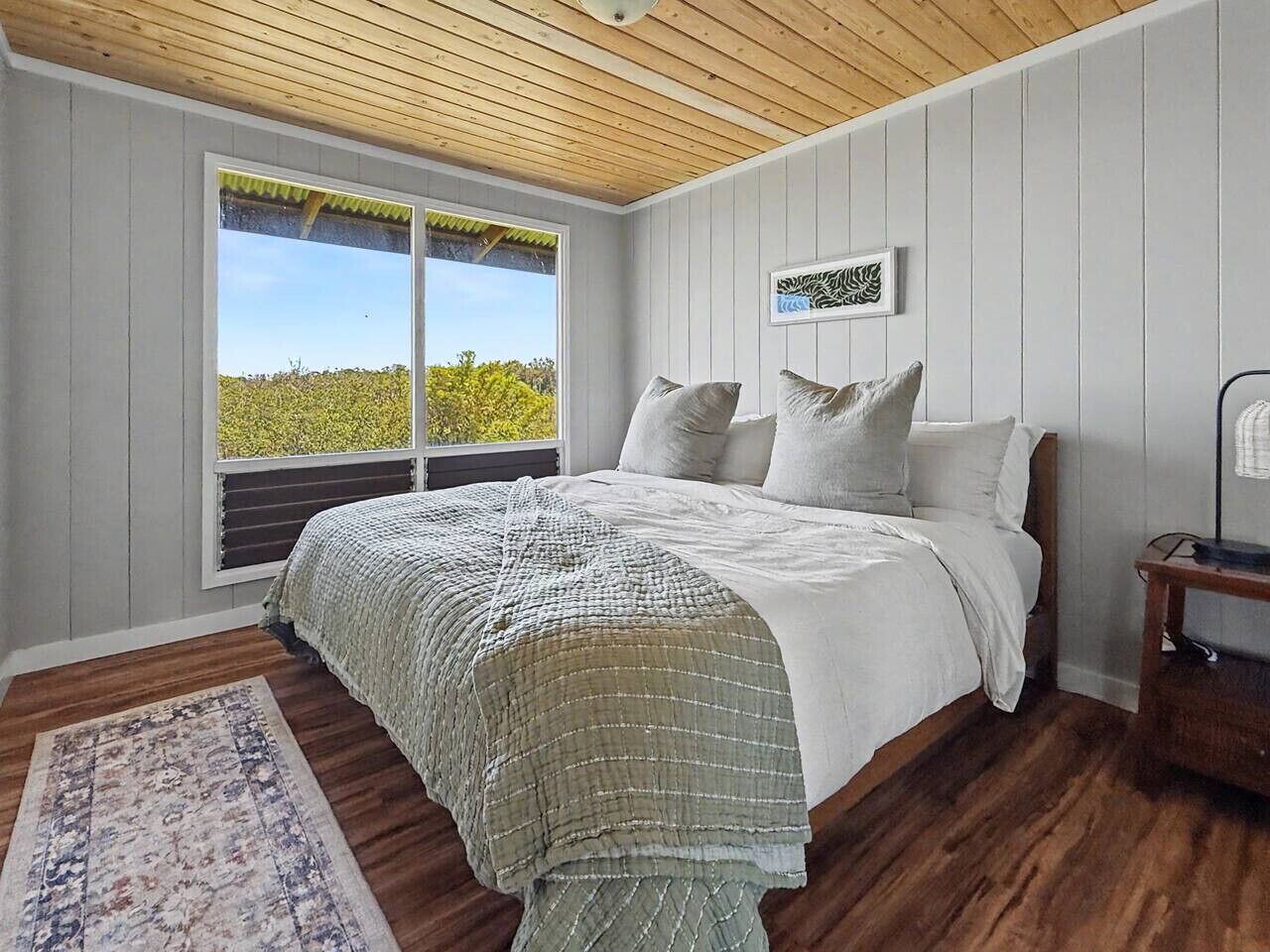 Une chambre à coucher avec un lit, une fenêtre donnant sur un beau paysage, un plafond en bois et une table de chevet.