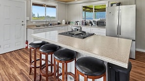 Une cuisine moderne dotée d’un grand îlot central, de tabourets de bar, d’appareils électroménagers en acier inoxydable et offrant une vue par les fenêtres.