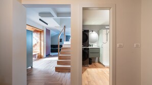 Un interno moderno con una scala in legno, una cucina con lavatrice e un bagno in vista.