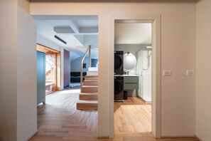 Un interior moderno con una escalera de madera, una cocina con lavadora y un baño visible.