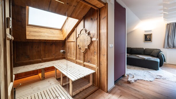 Un interno in legno con soffitto spiovente, una panca, un divano e un quadro appeso al muro.
