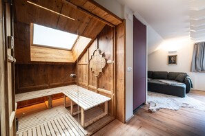 Een houten interieur met een schuine kap, een bank, een bankstel en een aan de muur bevestigd schilderij.