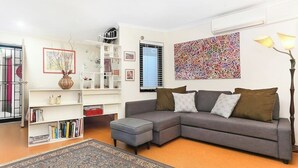 Un salon avec un canapé d’angle gris, un tapis à motifs, une bibliothèque et un grand tableau abstrait.