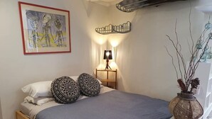 Une chambre à coucher avec un lit, des oreillers, une lampe, un tableau et un vase décoré de branches.