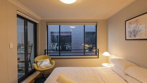 A hotel room with a bed, a chair, a window with a view of a balcony, and a nightstand with a lamp. - Chippendale Charmer in Ideal Location (Chippendale)