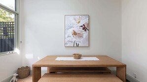 Una habitación con una mesa de madera, una cesta de mimbre y una obra de arte floral enmarcada en la pared.