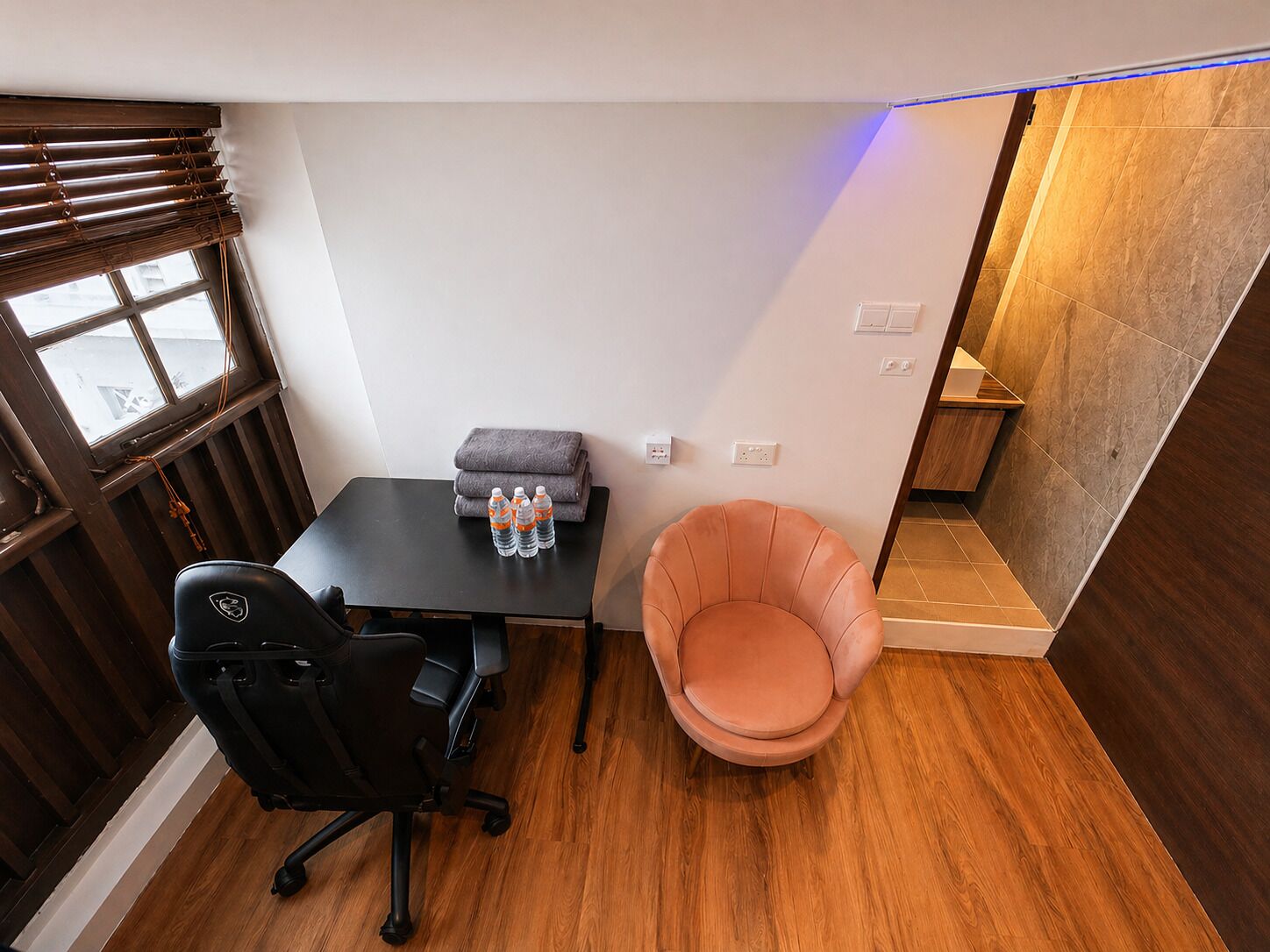 Una habitación pequeña con escritorio, silla y asiento acolchado.