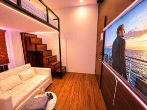 A modern interior with a sofa, wooden staircase, and a large TV screen displaying a cityscape. - Bugis Social- Newly Renovated (Singapore)