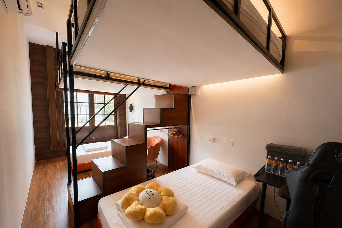 Una habitación de hotel pequeña con cama, una silla, un escritorio y una escalera.