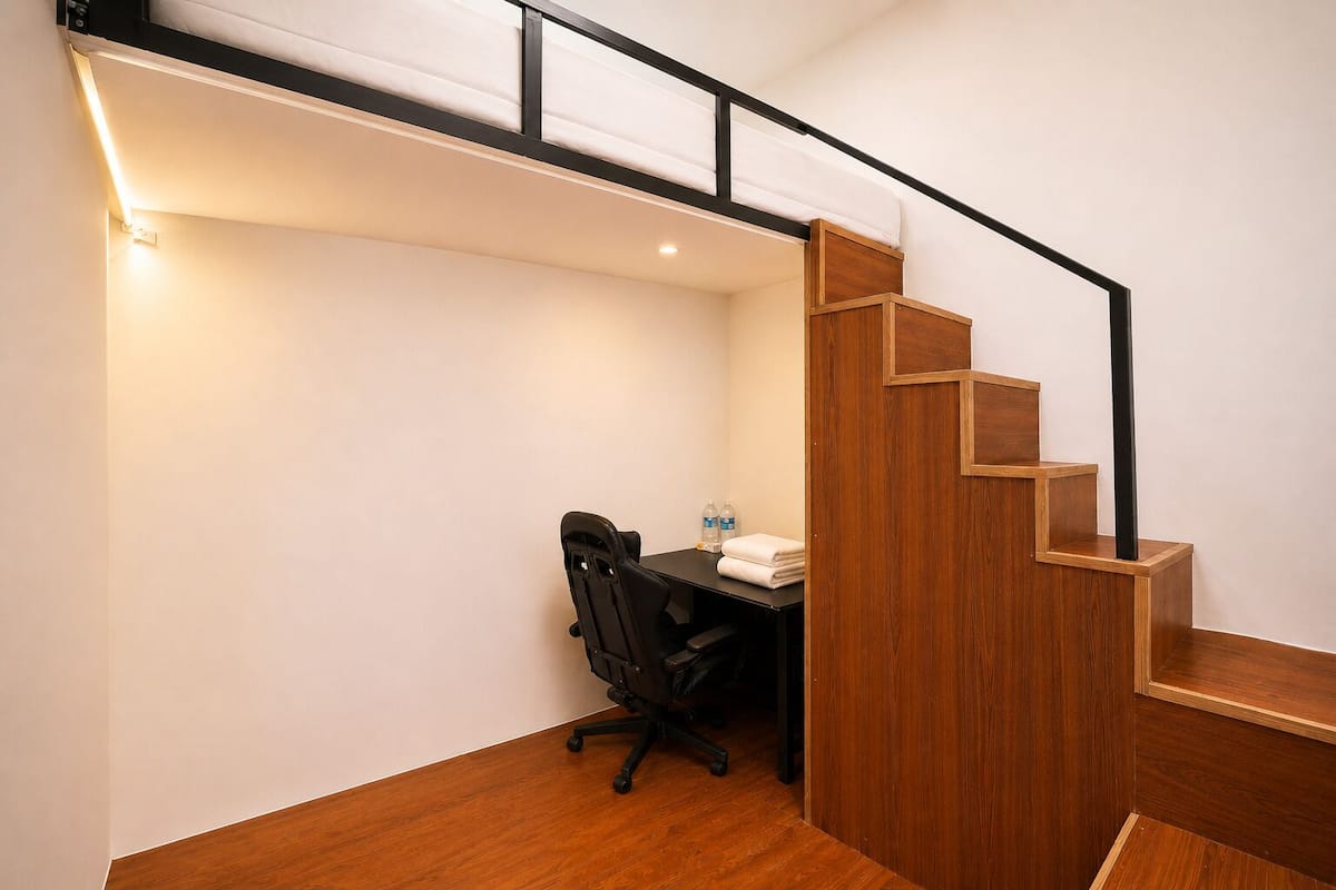 Una habitación pequeña con escritorio, silla y una escalera de madera.