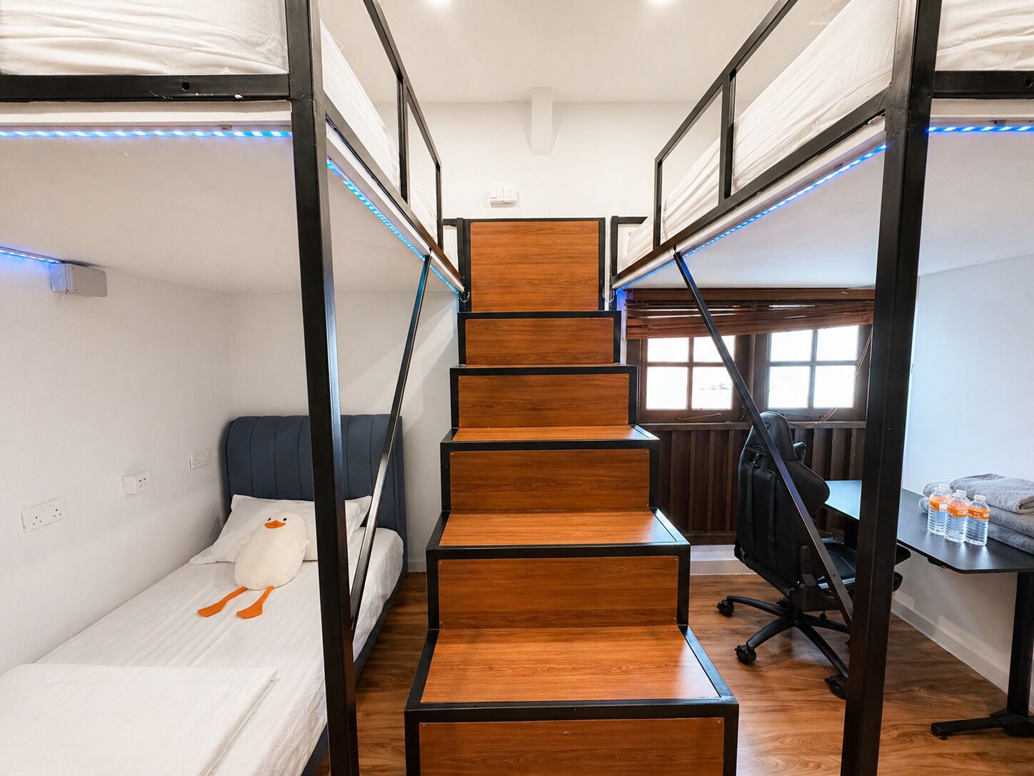 A compact room with bunk beds, a wooden staircase, a desk, and a chair.