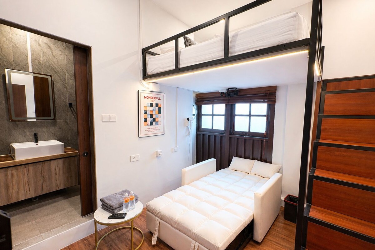 A compact bedroom with a bunk bed, a small bedside table, a single bed, a mirror, and a poster on the wall.