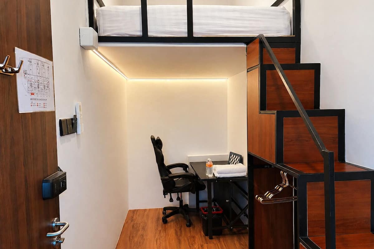 Una habitación compacta con cama tipo litera, un escritorio con silla, una mesita y una escalera.