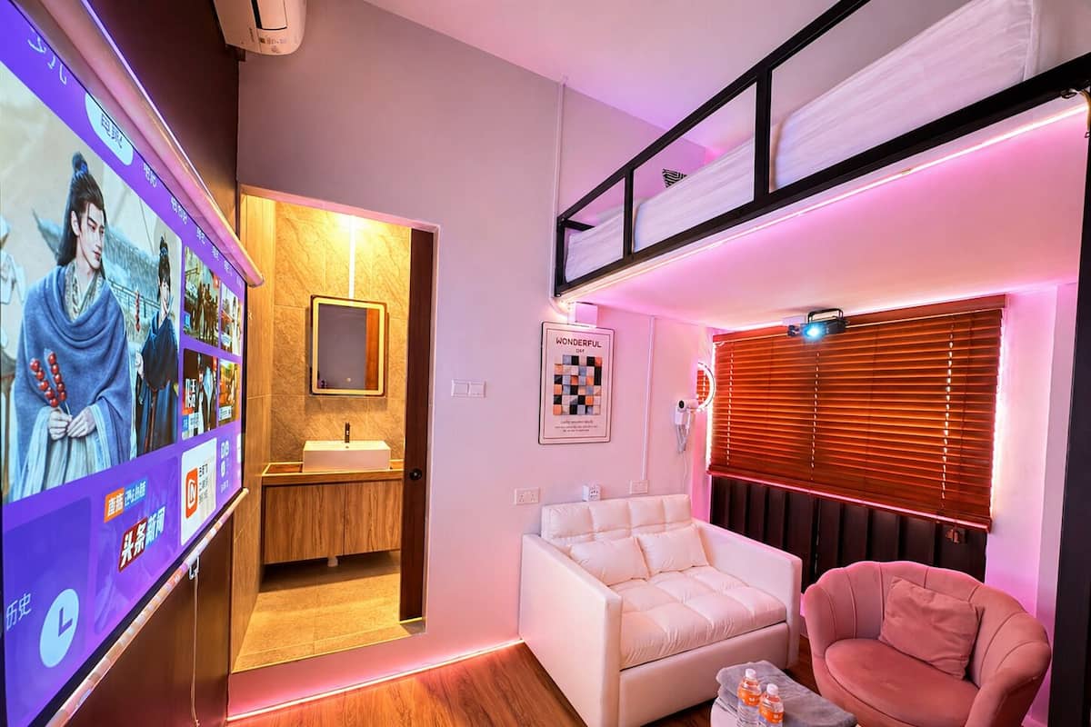 Una habitación de hotel moderna con televisión, un sofá, una silla, una mesita y una ventana con persianas.