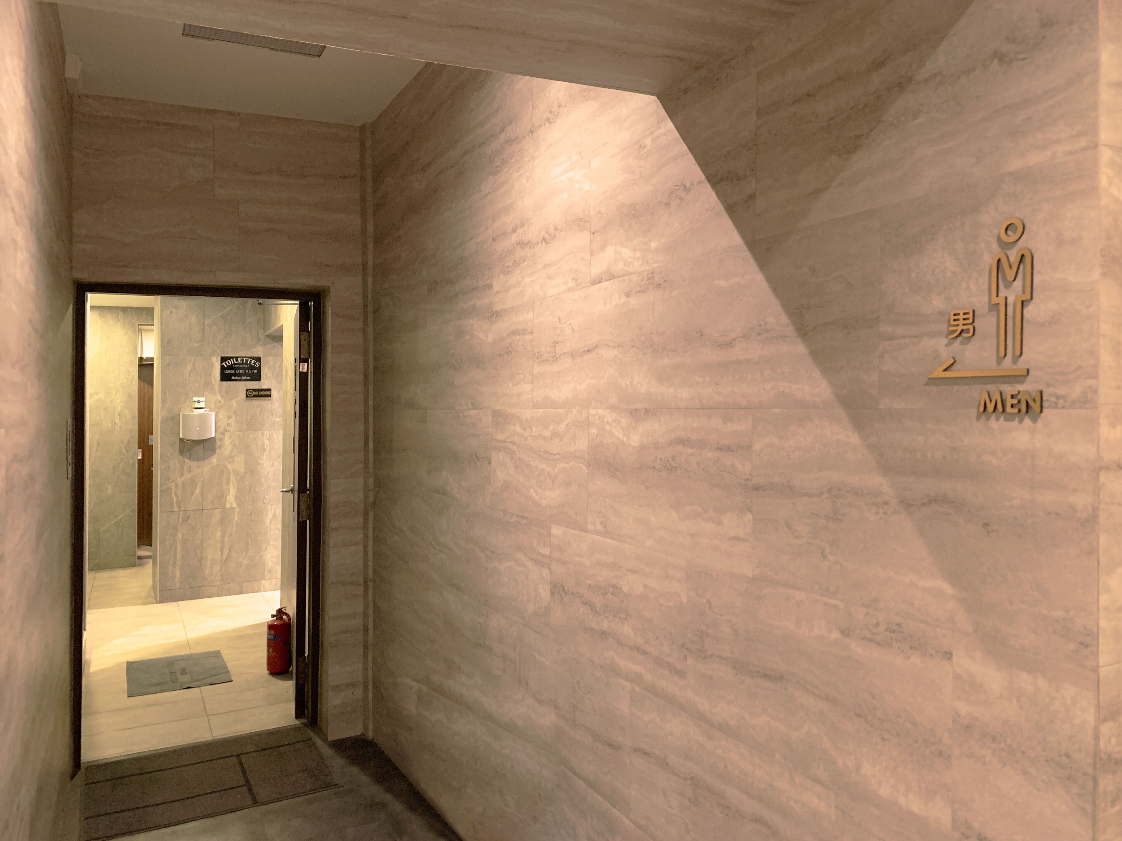 A hallway with a sign indicating the men's restroom, a fire extinguisher, and a door leading to a bathroom.