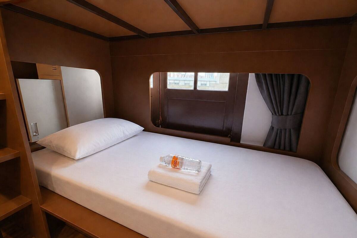 Una cama individual con colchón blanco, una mesita de noche pequeña, una botella de agua y una toalla doblada.