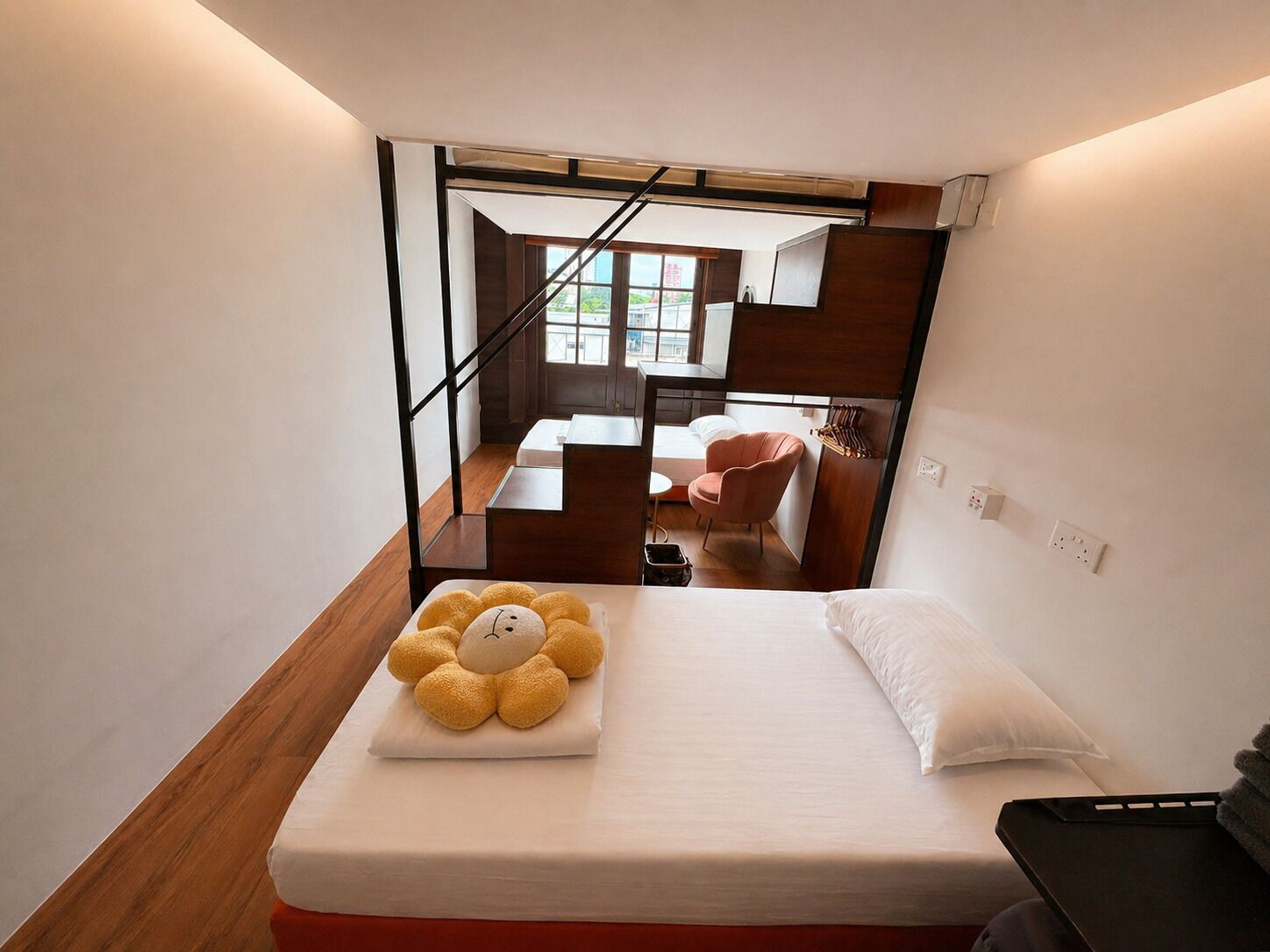 A compact hotel room with a bed, a small table, a chair, and a view of the outside.