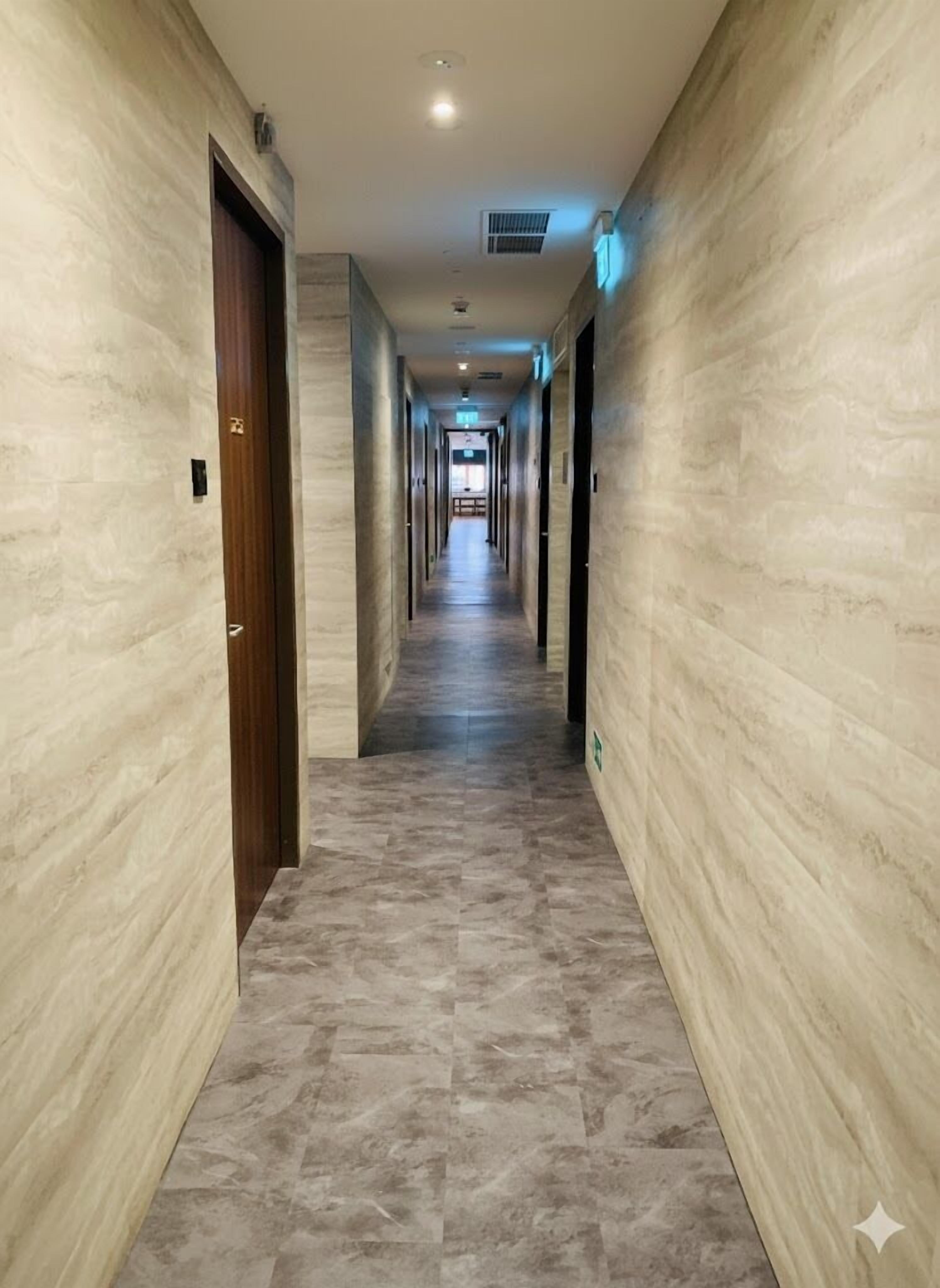 A long, narrow hallway with marble walls and a tiled floor, leading to a door at the end.