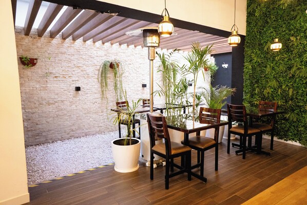 A dining area with wooden tables and chairs, potted plants, and hanging pendant lights. - PRANA (El Tambo)