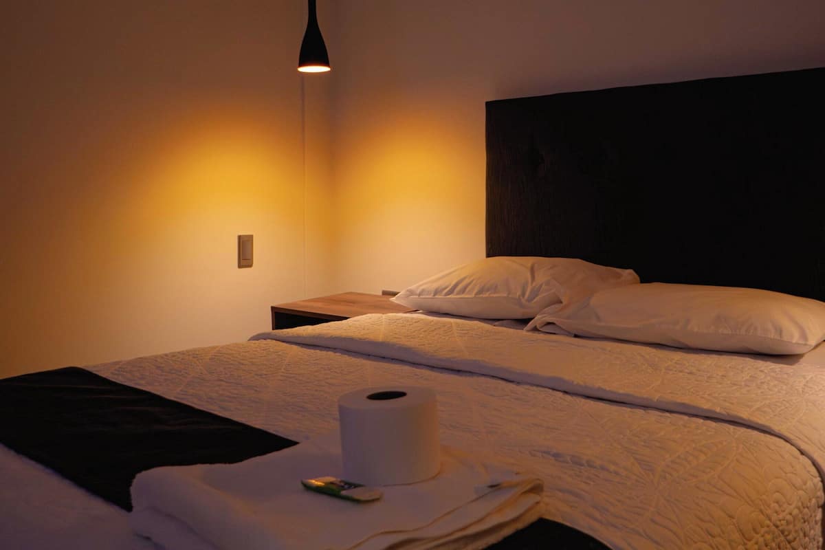 Una habitación de hotel con una cama, una mesita de noche, una lámpara y un aplique de pared.