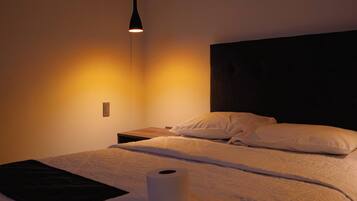 Una habitación de hotel con una cama, una mesita de noche, una lámpara y un aplique de pared.