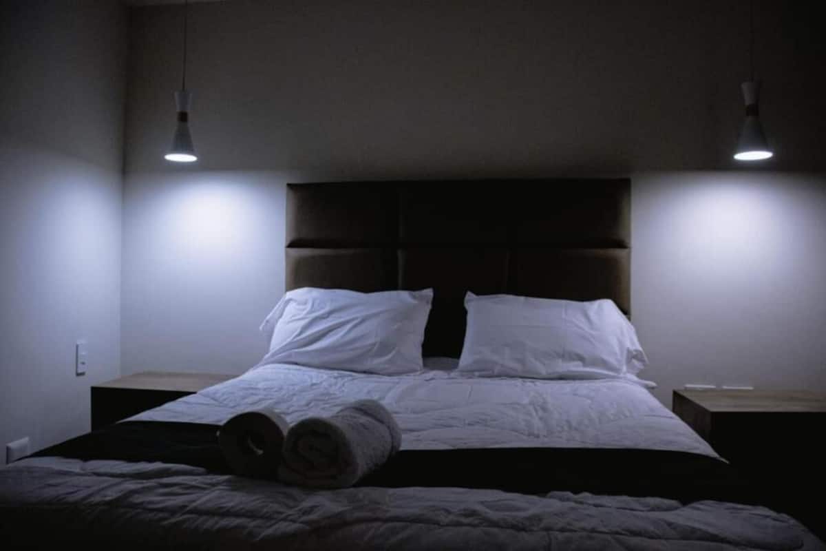 Un dormitorio con una cama, dos mesitas de noche y dos lámparas colgantes.