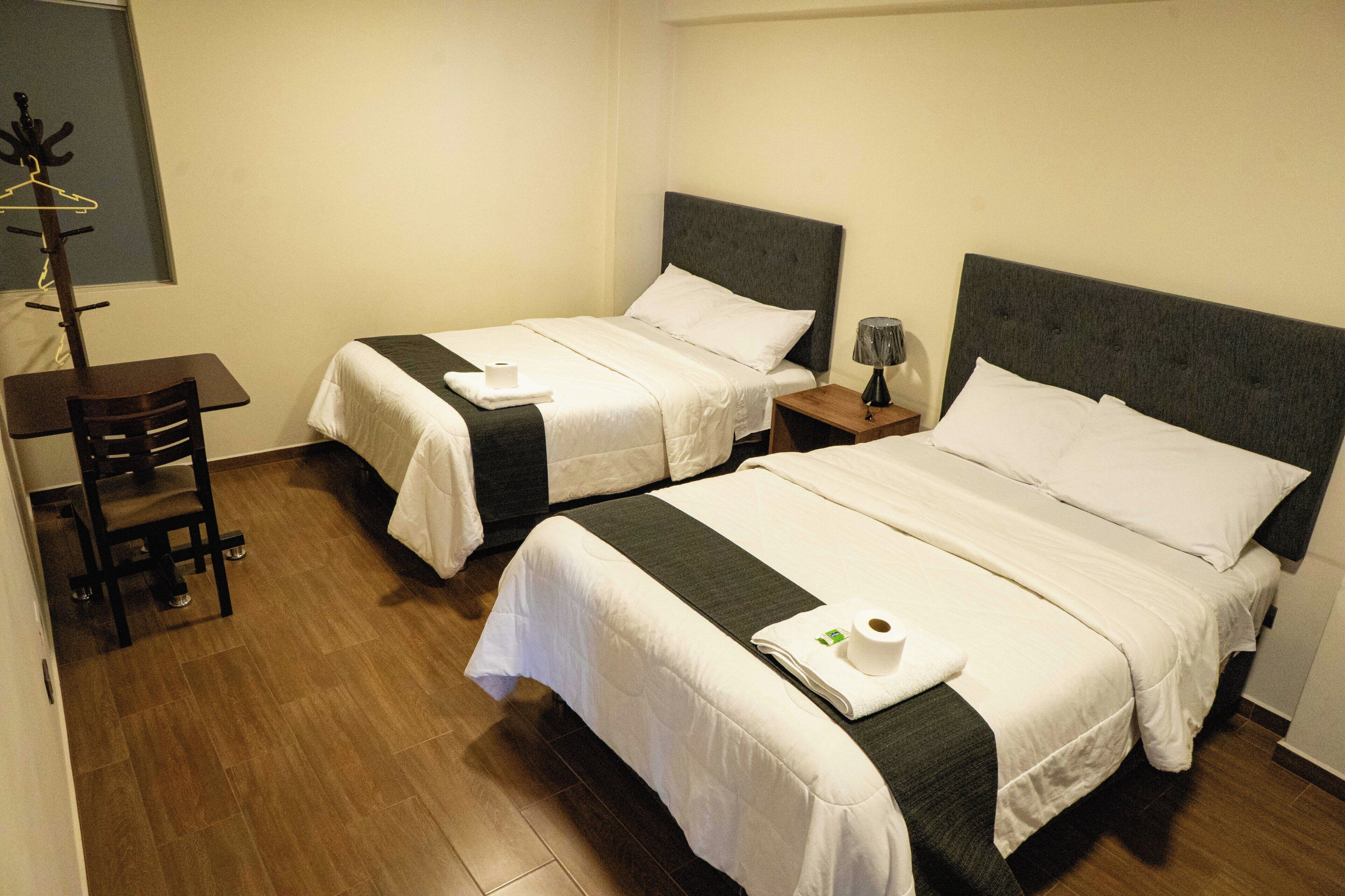 Two single beds with headboards, a wooden chair, a small table, and a lamp on a bedside table.