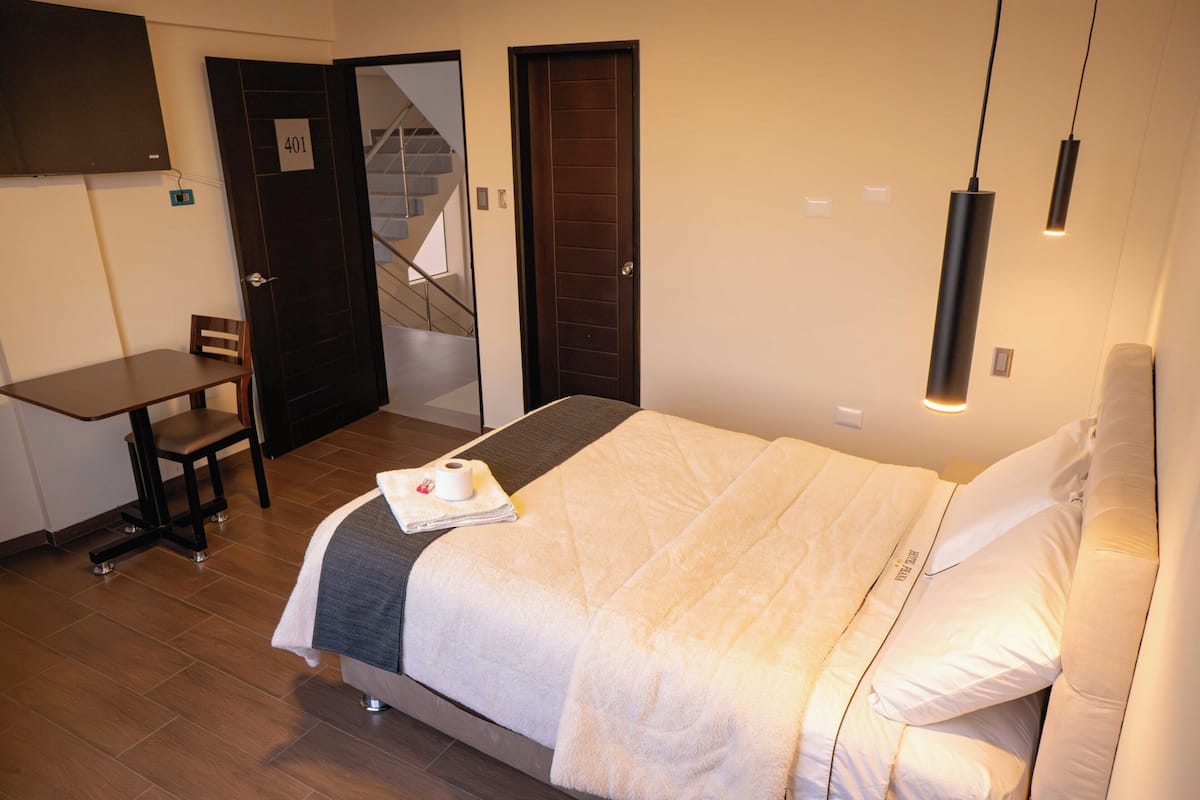 Una habitación de hotel con cama, escritorio, silla, puerta con el número y una escalera.