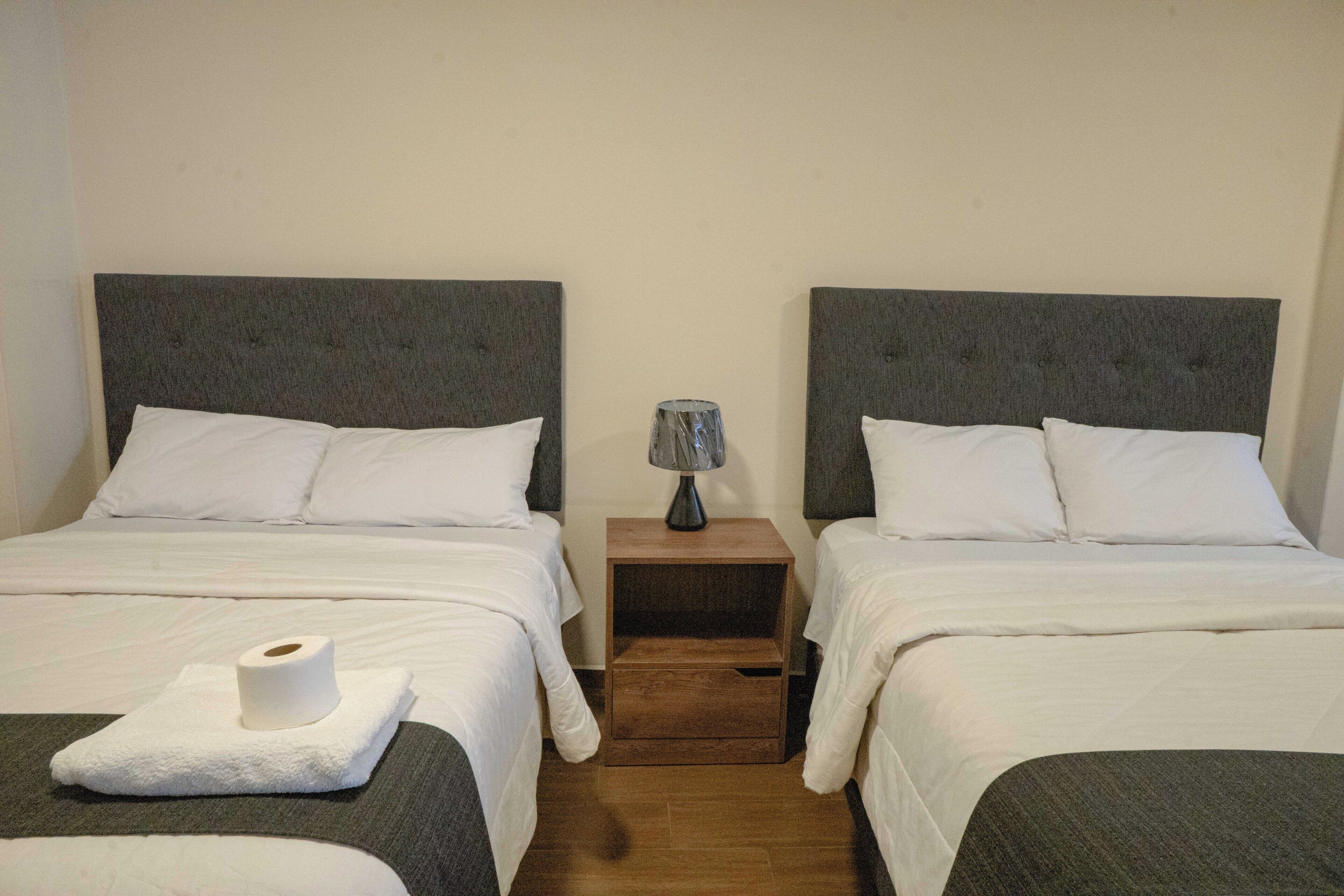 Una habitación de hotel con dos camas, una mesita de noche con lámpara y un rollo de papel higiénico en el suelo.