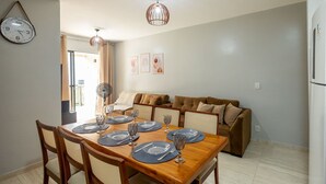 Un comedor con una mesa de madera dispuesta para cuatro personas, un sofá marrón y un reloj en la pared.