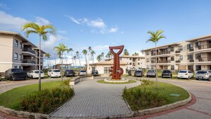Un estacionamiento con una escultura central, rodeado de palmeras y edificios de varios pisos.